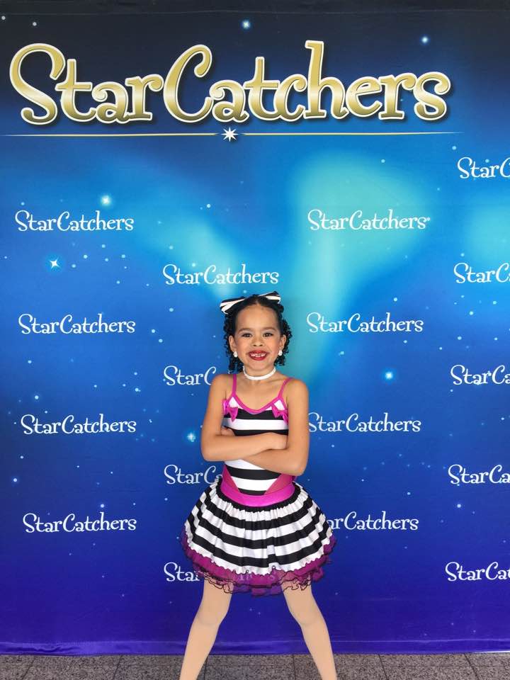 competitive dancer in dance costume in front of a sign saying Star Catchers